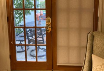 Custom roller shade partially raised on left patio door, showing patio and outdoor seating area through the window.