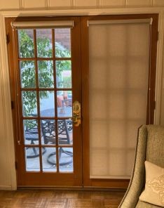 Custom roller shade partially raised on left patio door, showing patio and outdoor seating area through the window.
